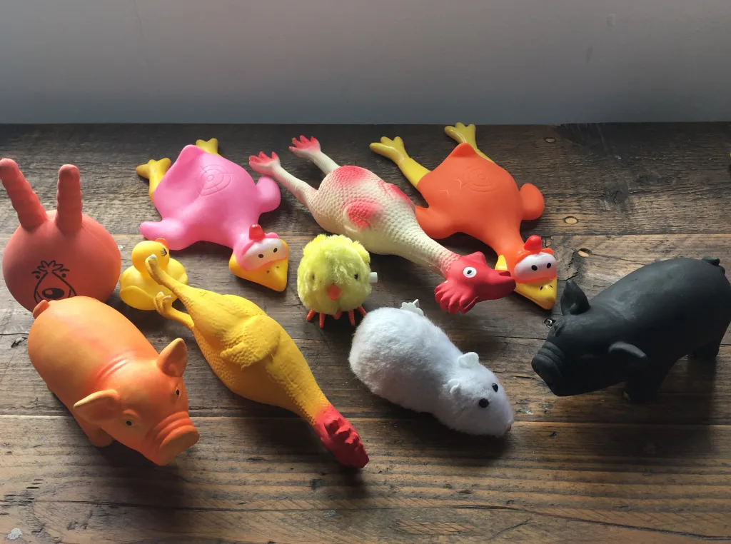 A collection of colorful rubber and plush toy animals including pigs, chickens, and a mouse, arranged on a wooden floor